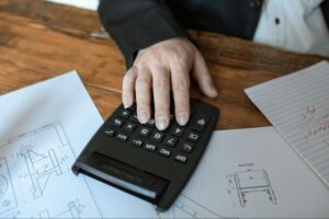 Construction professional calculating project costs using a calculator over technical drawings.