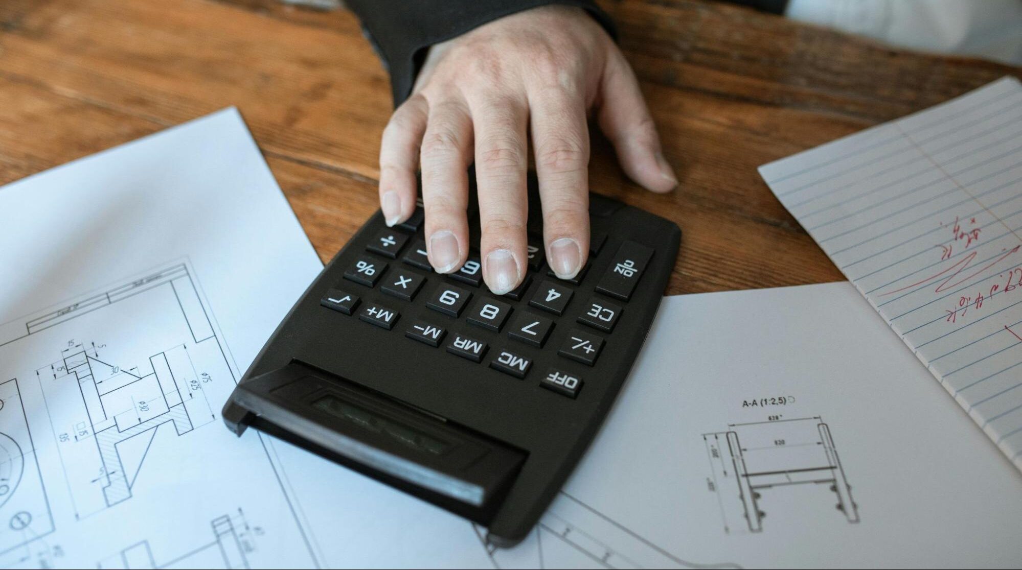 Construction professional calculating project costs using a calculator over technical drawings.