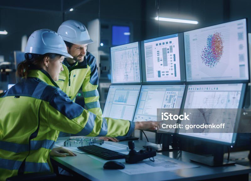 Two people reviewing a detailed digital planning and task schedule on multiple computer screens.