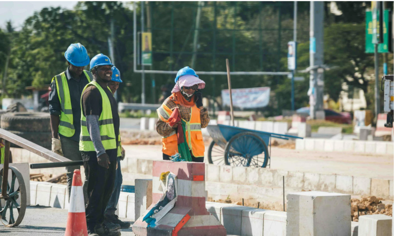 Construction crew working on roadside project with safety barriers, equipment, and on-site coordination.