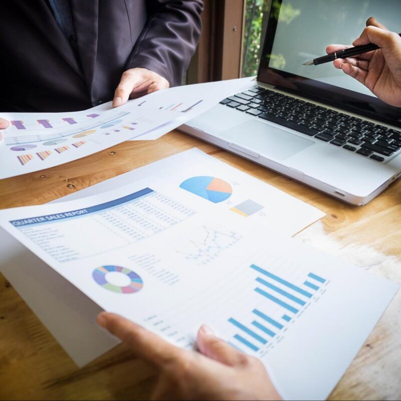 Business leaders reviewing multiple financial and operational reports beside a laptop, highlighting conflicting data during expansion planning.